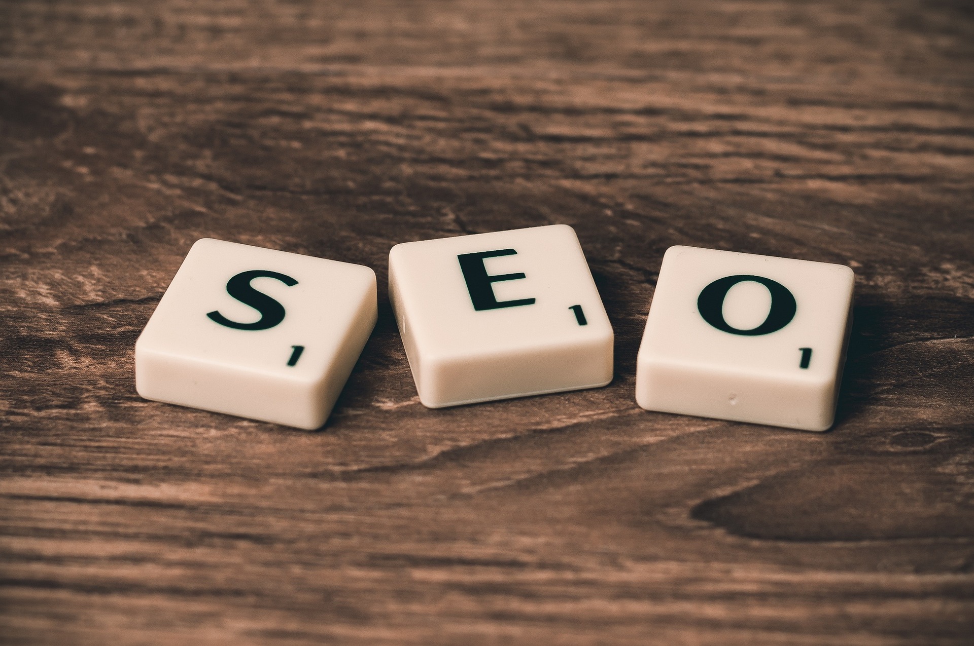 three scrabble letters spelling SEO placed on a brown wooden table top
